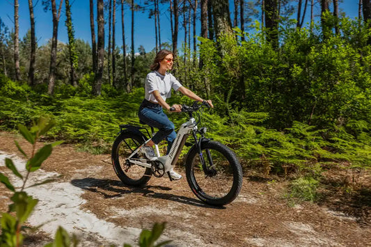 Woman riding white Shengmilo MX06 e-bike on forest trail exploring nature with electric bikes in sunny weather