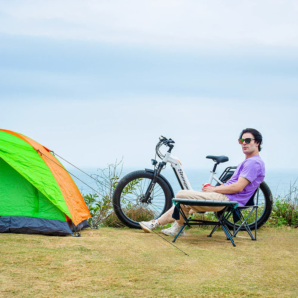 Unleashing the Adventure The Shengmilo MX06 Electric Bike parked beside a camping tent with a man relaxing on a chair outdoors