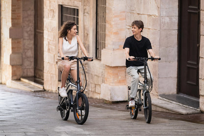 Two people riding DYU T1 20 Inch Foldable Electric Bike with magnesium alloy frame and dual disc brakes on city street